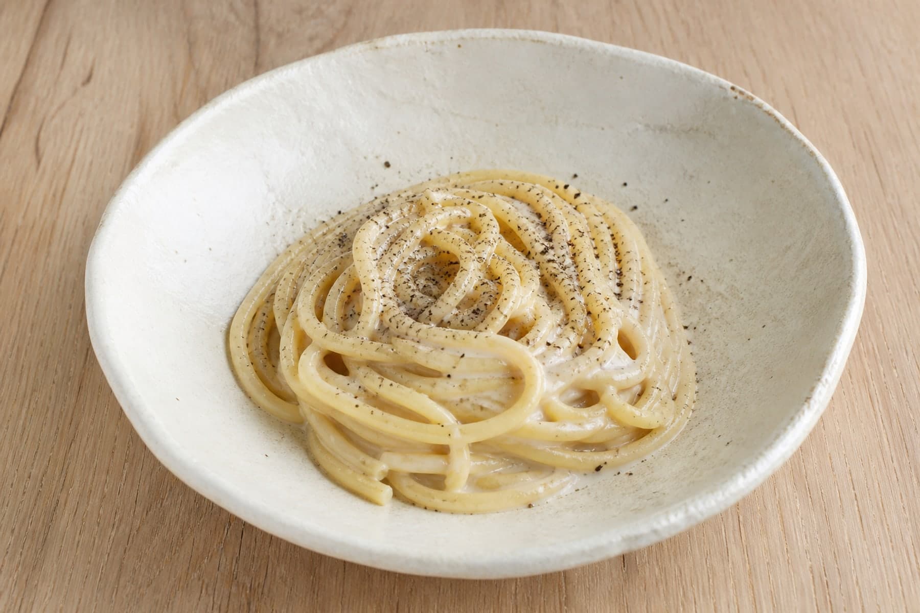 Tonnarelli cacio e pepe with black pepper in a pale handmade bowl