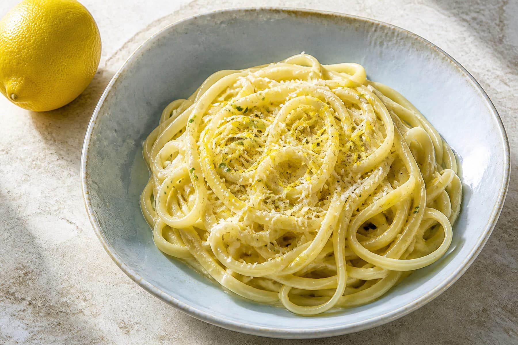 Silky linguine al limone with lemon zest and Parmesan in a pale blue ceramic bowl