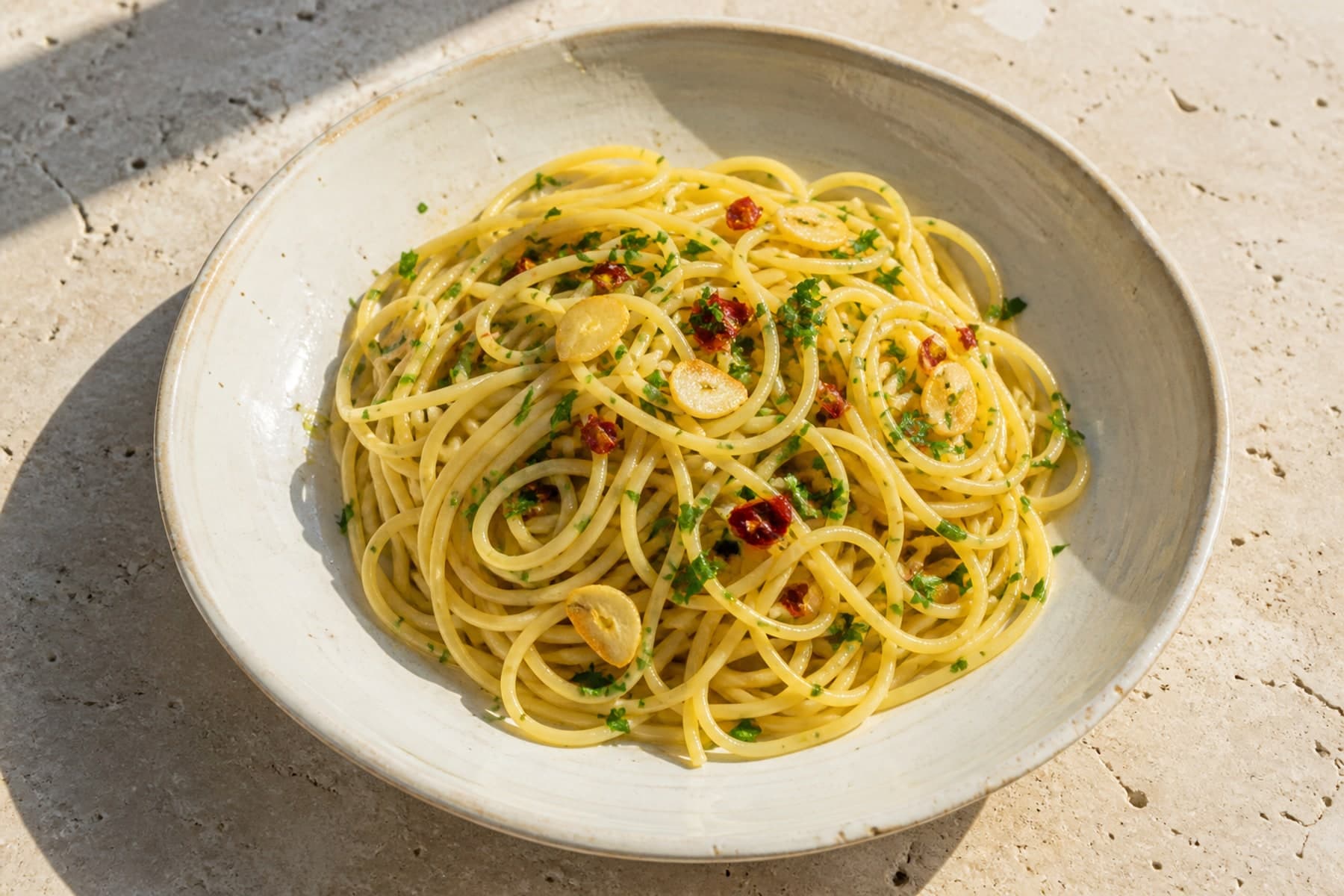 Spaghetti aglio e olio with sliced garlic chilli and parsley on a sunlit ceramic plate