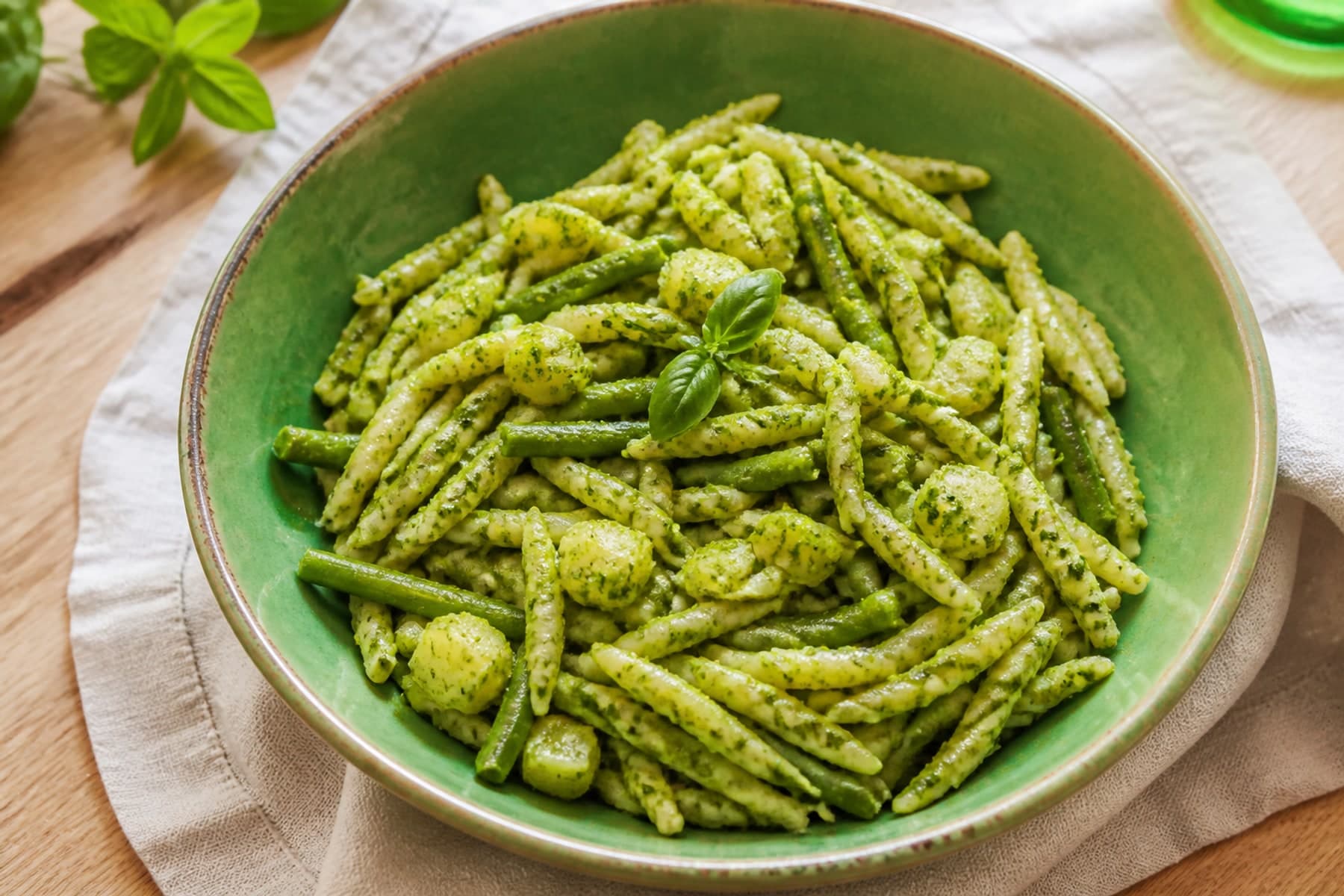 Trofie pasta with bright basil pesto green beans and potato in a handmade green bowl