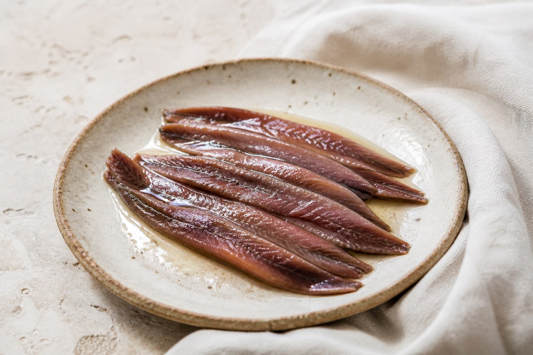 Silvery brown cured anchovy fillets glistening with olive oil on a small plate