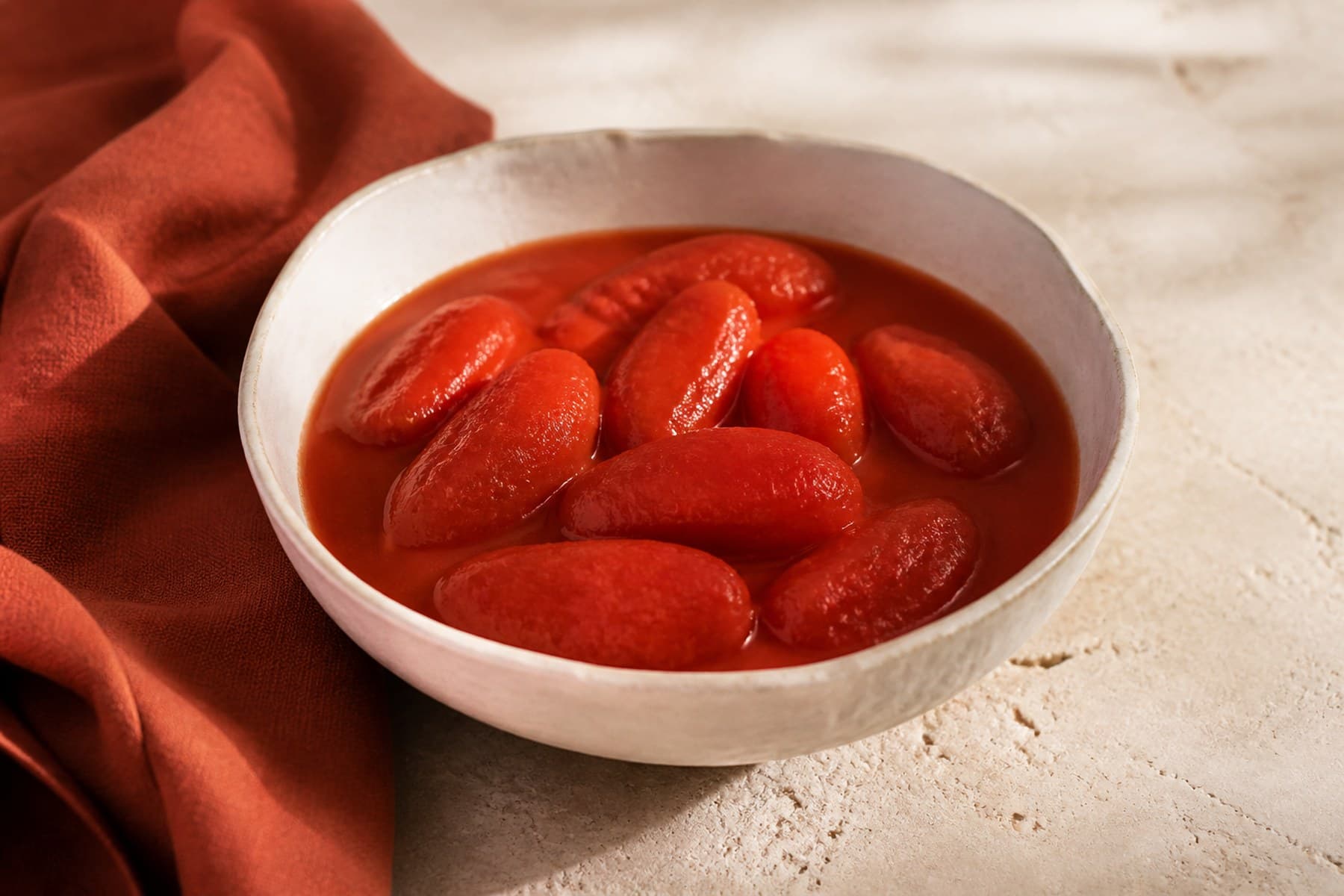 Whole peeled plum tomatoes and thick red juice in a plain ceramic bowl