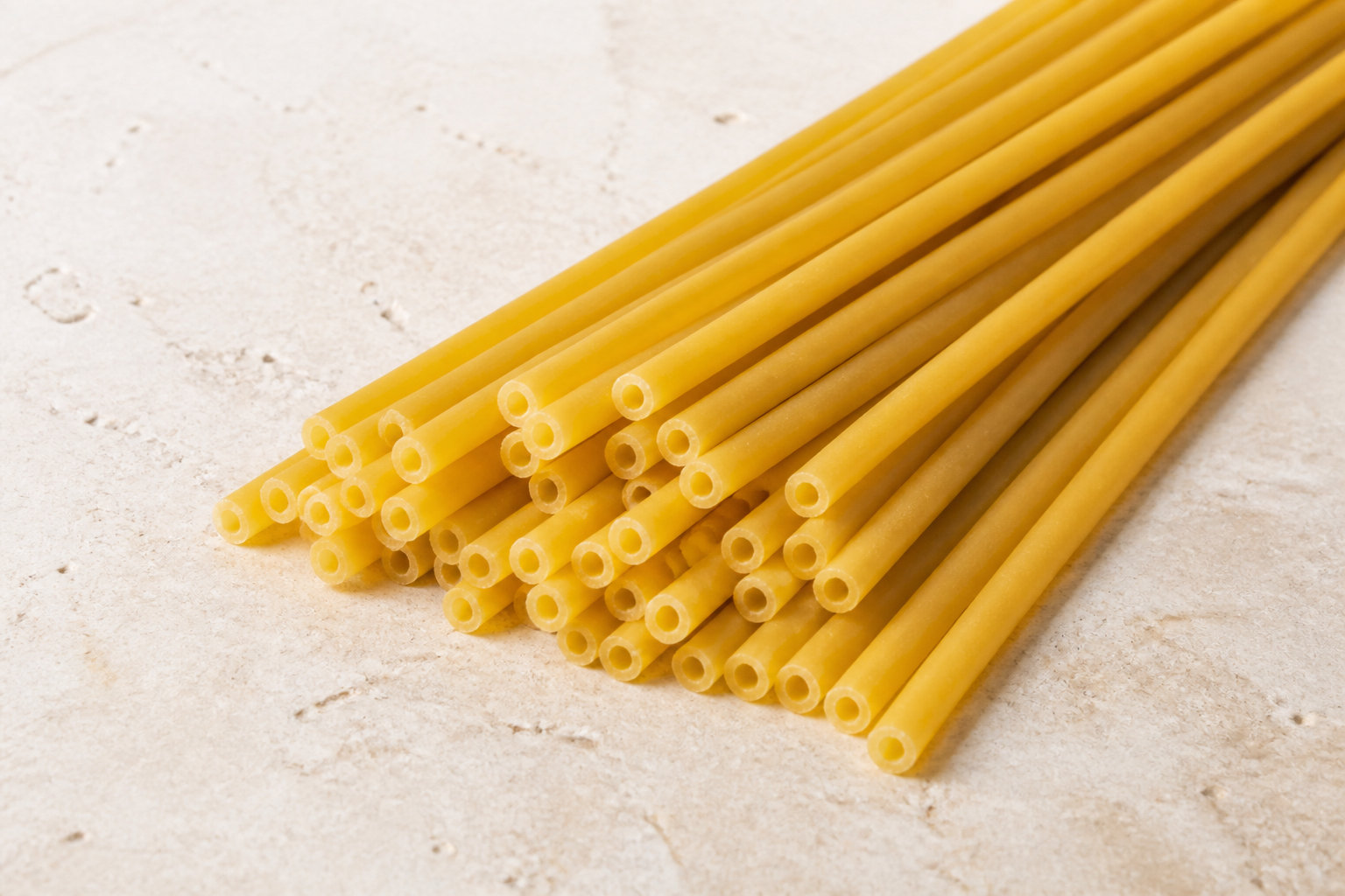Long dry bucatini strands showing the narrow hollow centre through each thick tube
