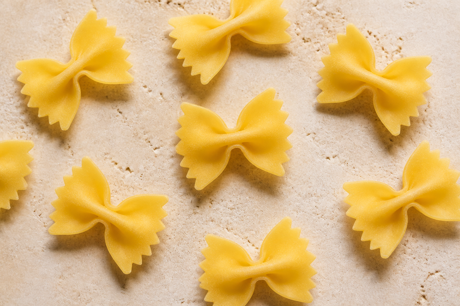 Dry farfalle pasta showing crimped wings and thick pinched centres on pale stone