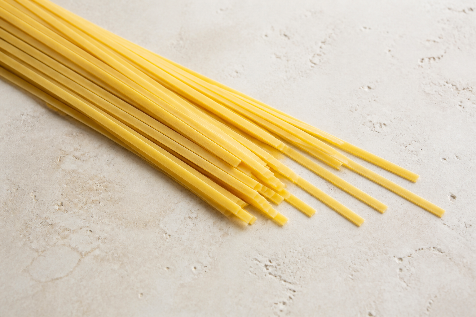 Long dry fettuccine showing its flat medium-width ribbon shape on pale stone