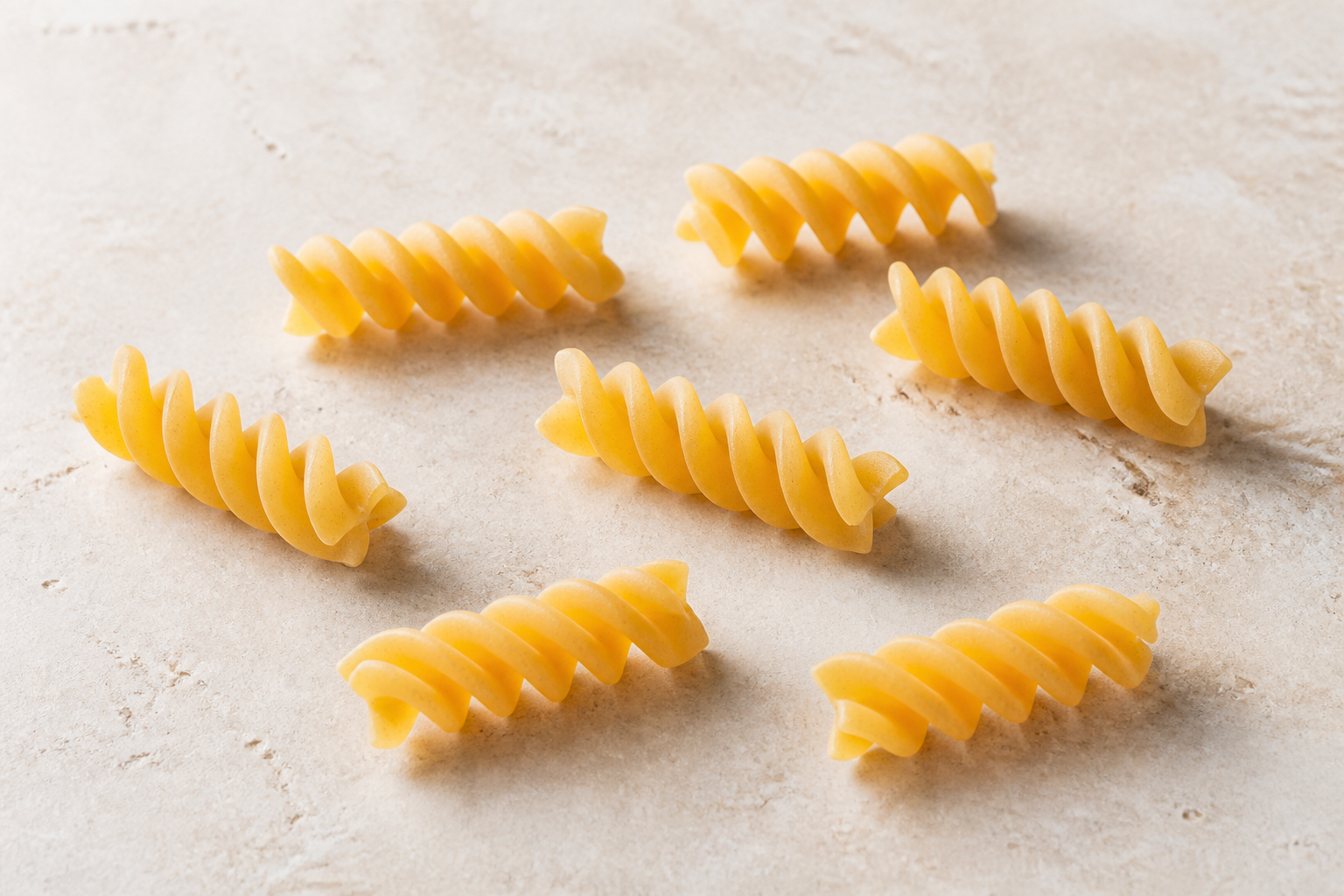 Dry fusilli pasta showing its short corkscrew spirals on pale stone