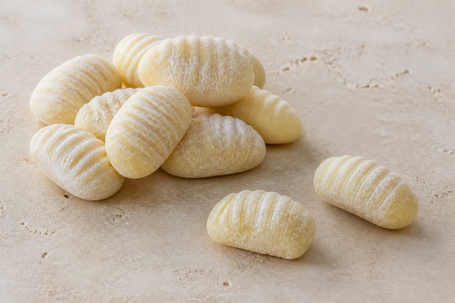 Uncooked ridged potato gnocchi dumplings showing their solid pillow shape on pale stone