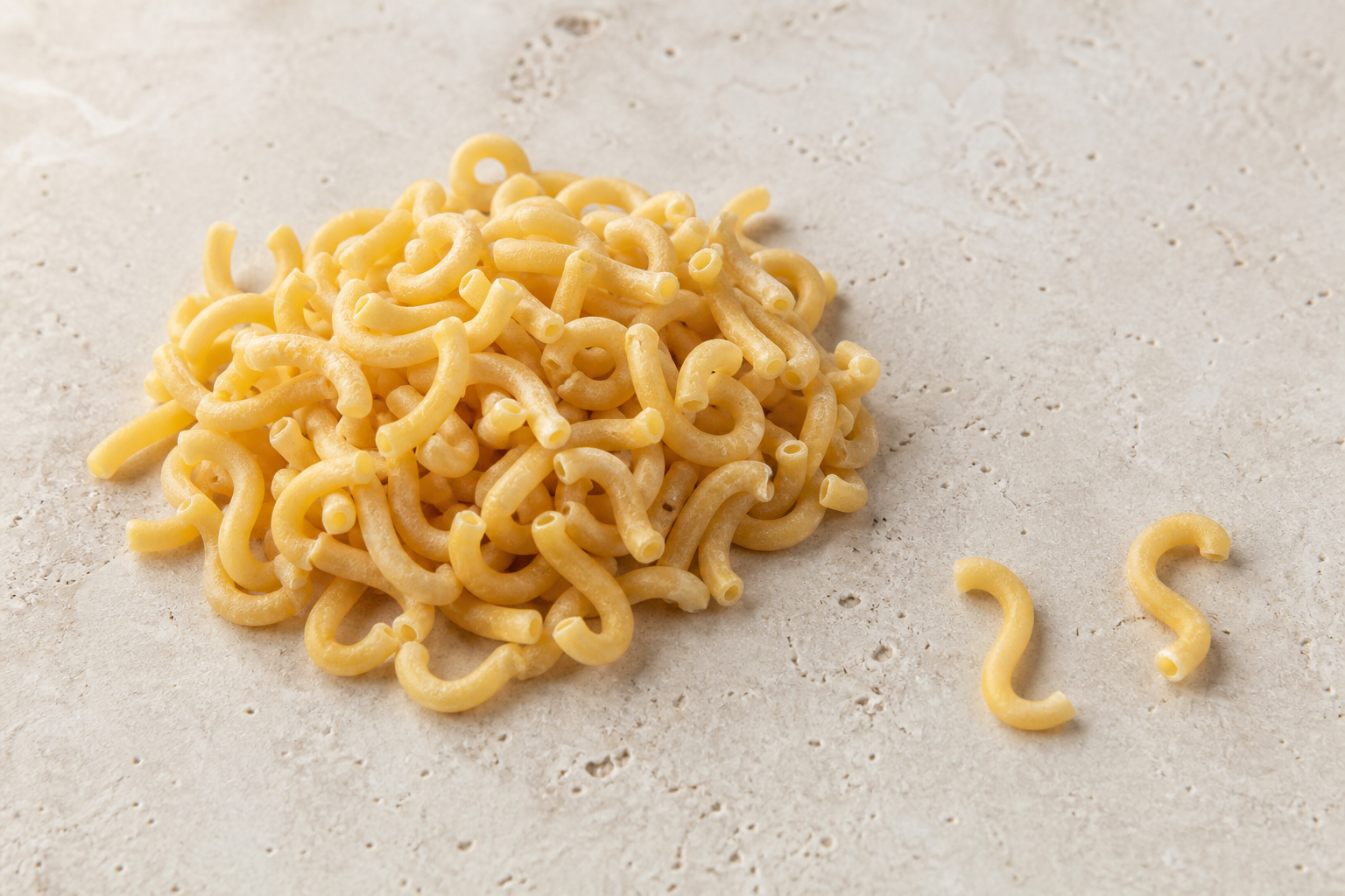 Dry Gramigna pasta showing tiny hollow hooked tubes and open ends on pale stone