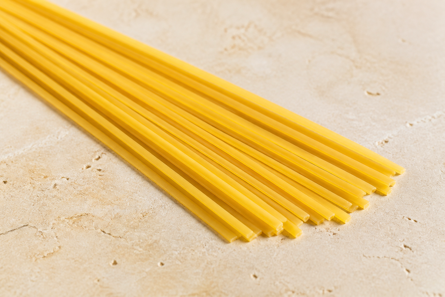 Long dry linguine strands showing their narrow flat ribbon shape on pale stone