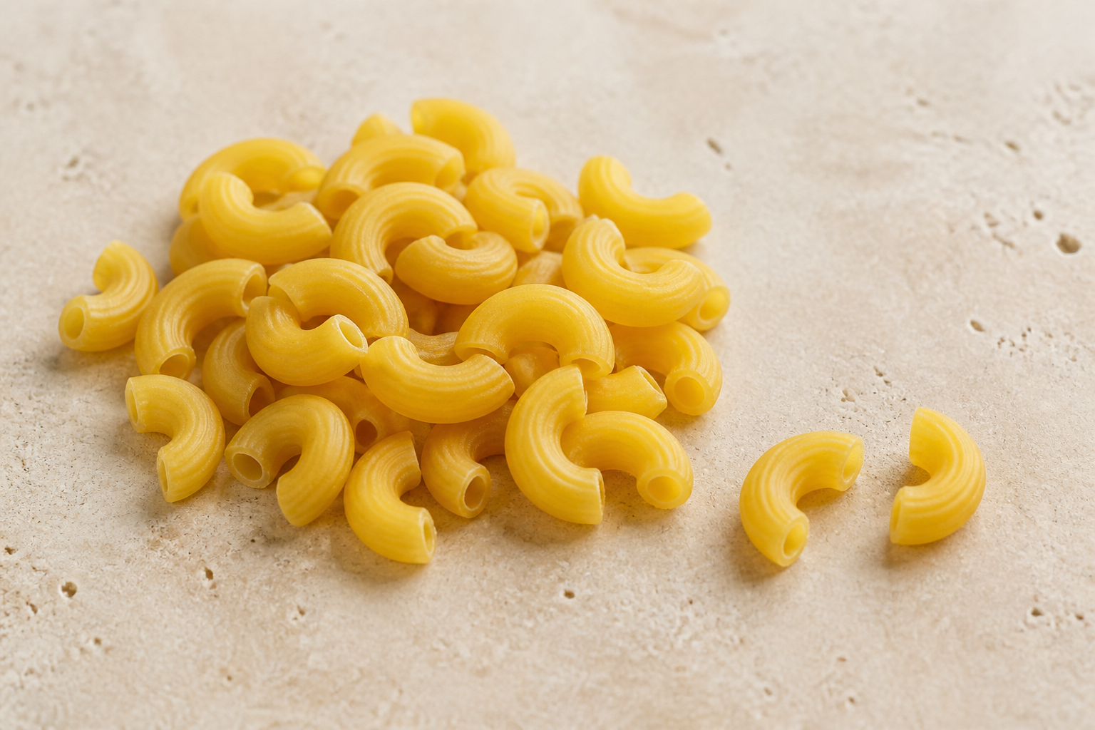 Dry elbow macaroni showing intact curved hollow tubes and round open ends on pale stone