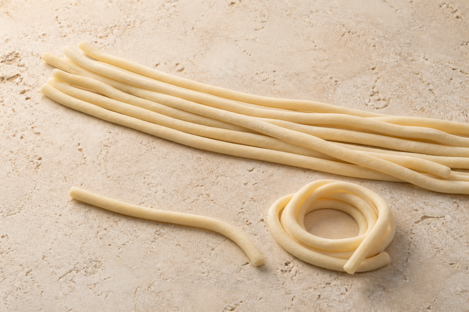 Fresh hand-rolled Tuscan pici showing thick irregular solid strands on pale stone