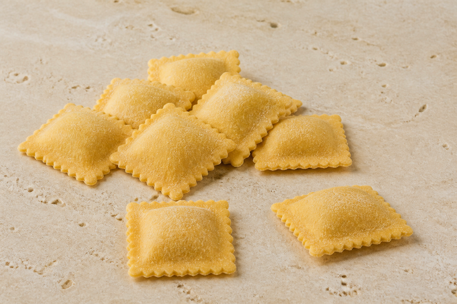 Fresh square ravioli showing centred filling mounds and fluted sealed borders on pale stone