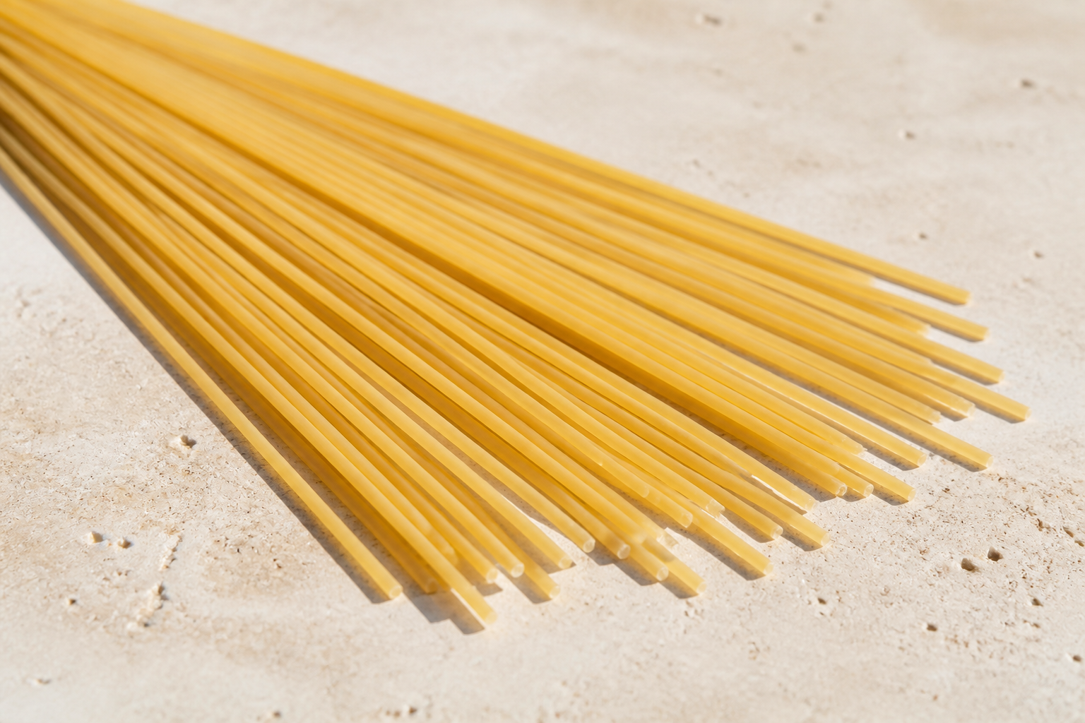 Long dry spaghetti strands showing their slim round solid shape on pale stone