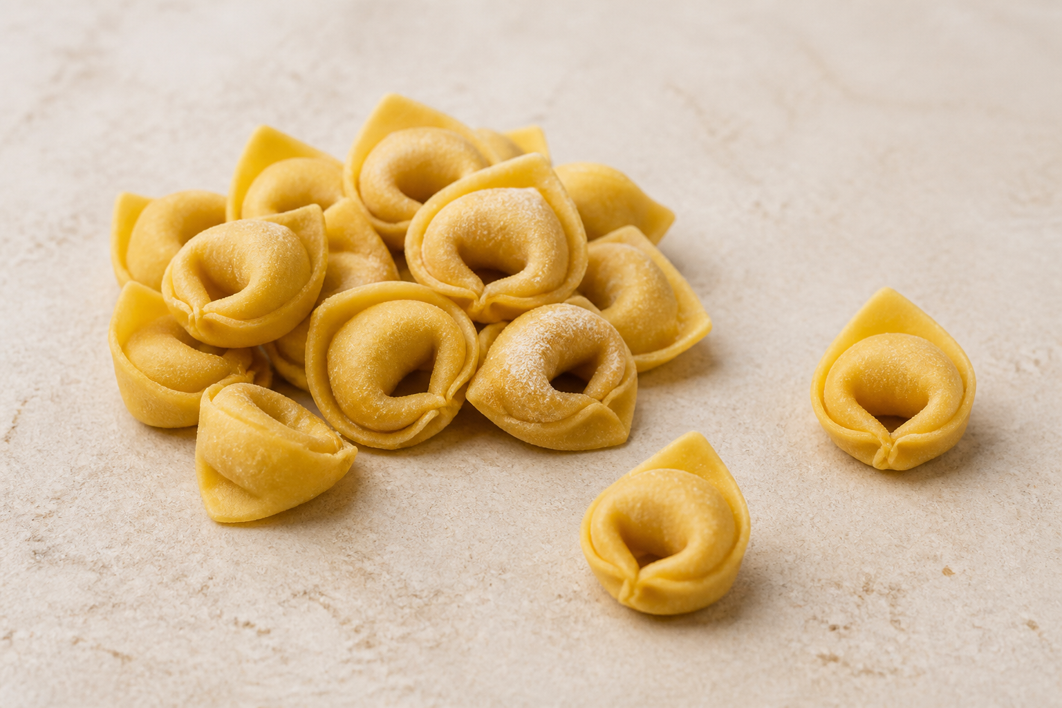 Fresh small tortellini showing compact filled rings, joined corners and raised triangular flaps on pale stone
