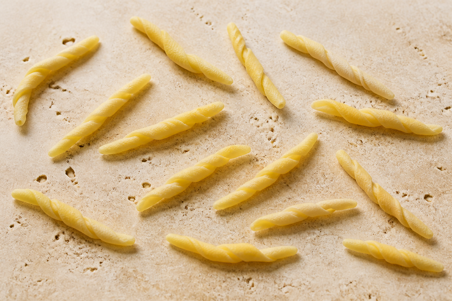 Dry Ligurian trofie pasta showing short tapered hand-rolled twists on pale stone
